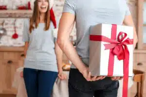 Happy young man giving Christmas present that gives back to his girlfriend at home