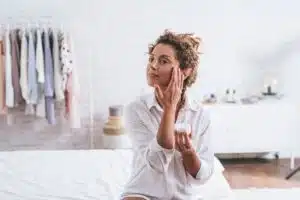 Pretty smiling Caucasian woman applying a skin cream to her face during her morning routine.