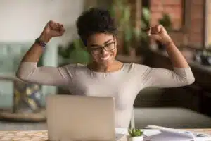 Black woman feeling triumphant while looking at laptop
