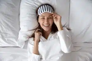 A woman wearing a striped eye mask wakes up looking refreshed from getting quality sleep