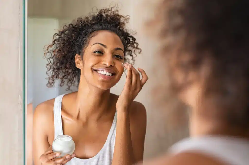 Black woman cares for her beautiful ski by applying product on her face.