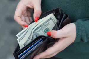 Woman hands with red nails holds black leather wallet with many US hundred dollars bills. Concept of salary earnings or money counting.
