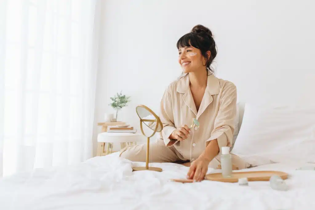 A woman doing skincare while sitting on bed.