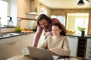 A couple in the kitchen in front of laptop laugh over financials.