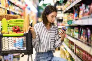 A young woman with a grocery cart shops in the supermarket and reads the labels
