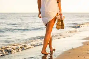 A woman walking solo along a beach holding her shoes