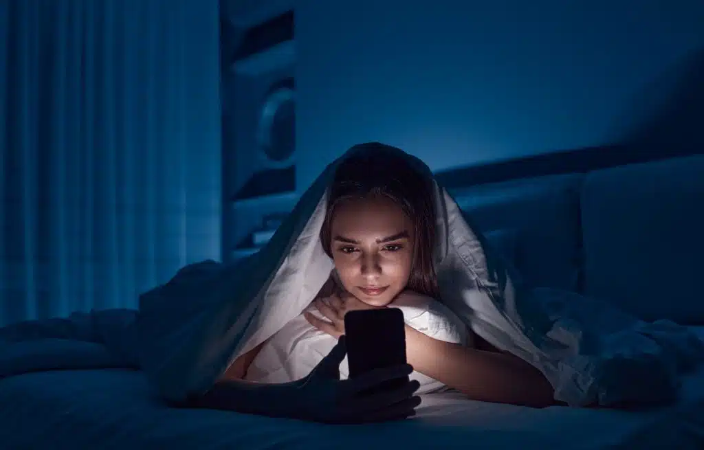 A young woman up late scrolling on her phone in bed