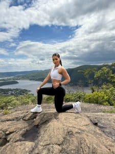 Erika Peralta kneeling on a mountaintop while wearing workout clothes.