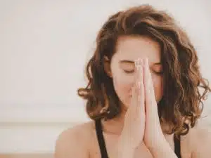 A woman with shoulder-length curly brown hair giving thanks while meditating