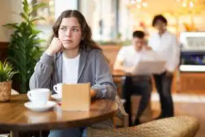 Young woman sits at a table in a cafe pondering who she is.