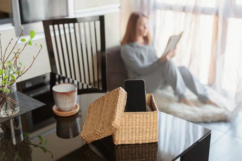 A woman in a window seat reads book while her phone is in a separate box indicating a digital detox.