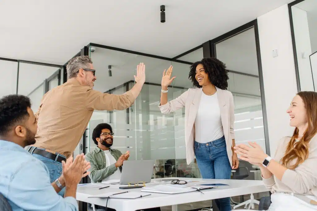 A diverse group of professionals in a modern office celebrate with high-fives.