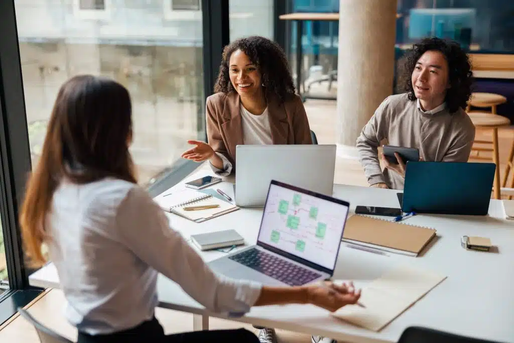 A diverse group of colleagues gathered around a table with their laptops working.