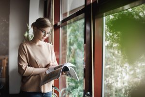 A young woman reads a magazine by a window