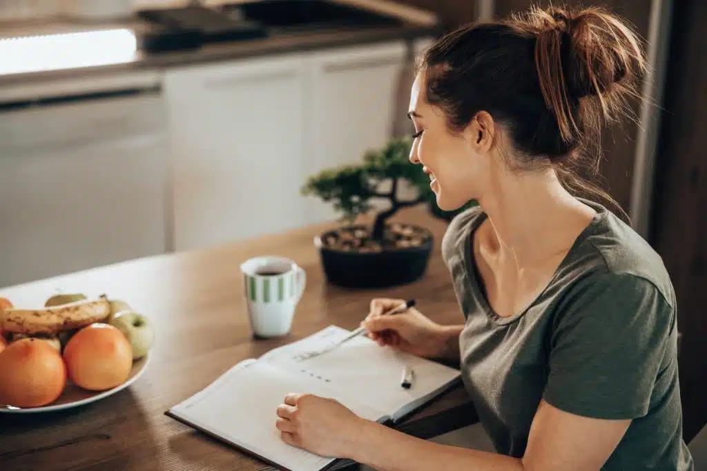 A woman at kitchen table with a cup of coffee making her to-do list