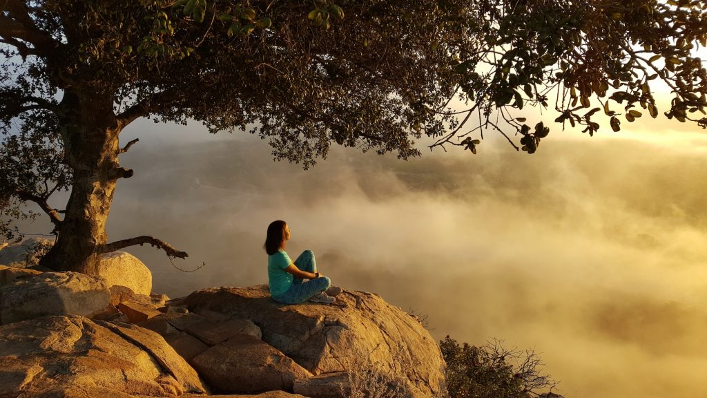 A woman sits on a rock under a tree looking out over a cloudy landscape at Rancho La Puerta.