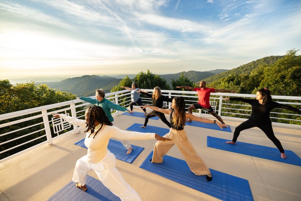 A group of women do yoga on the outdoor deck at the Art of Living Retreat Center