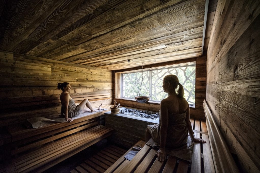 A wood sauna with two women relaxing and looking out the window.