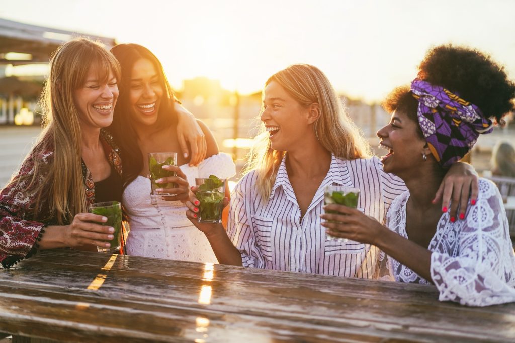 a group of four friends (multiracial) enjoy mocktails with the sun setting behind them
