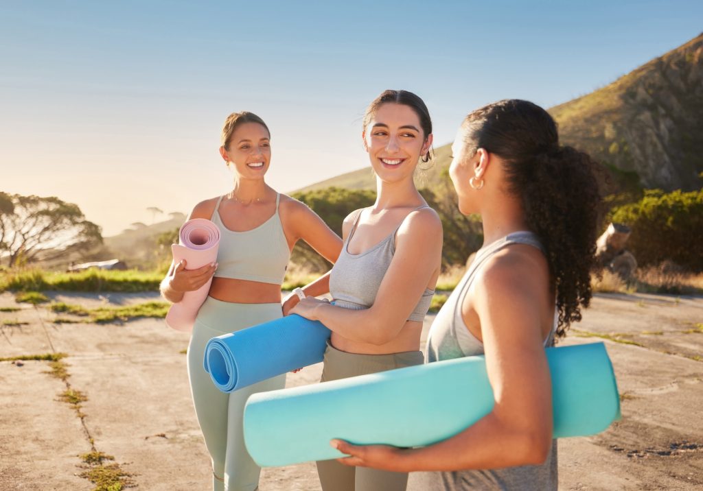 Three young woman outside with yoga mats, enjoying a wellness getaway