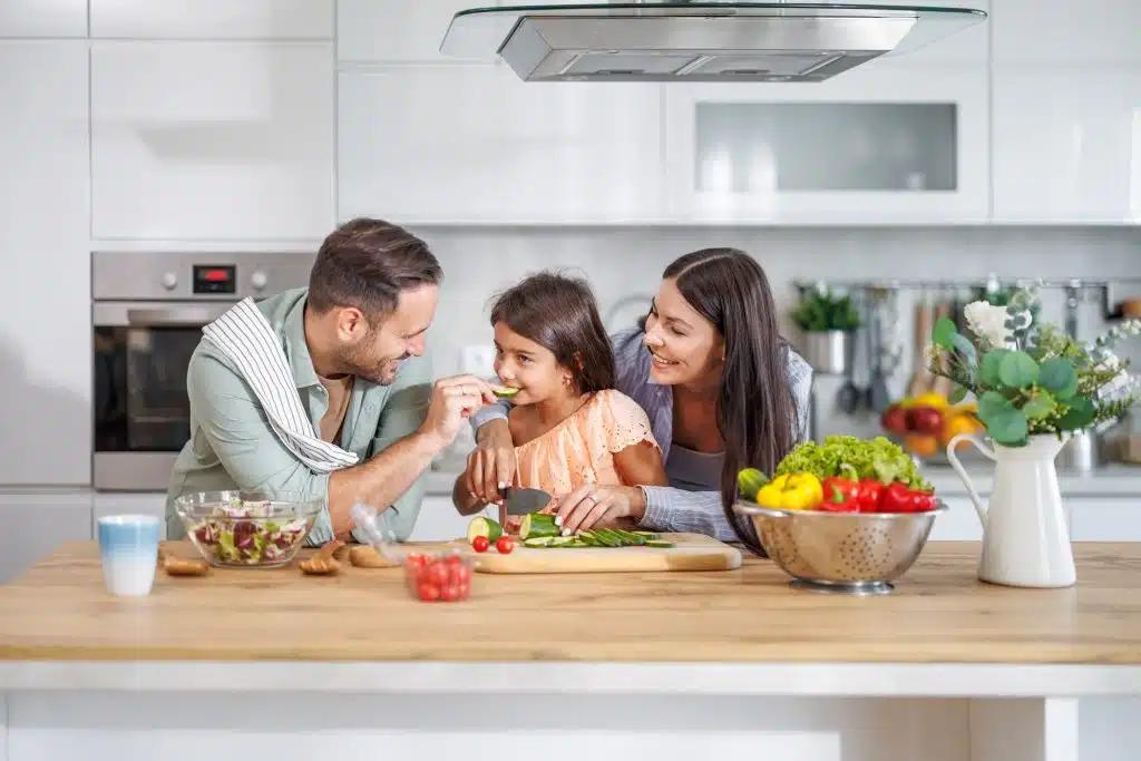 A happy family of three enjoy a healthy meal in a bright, modern kitchen.